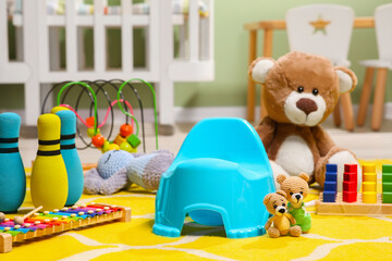 Light blue baby potty, teddy bear and many other toys in room. Toilet training