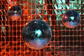 Shiny disco balls against foil party curtain under color lights