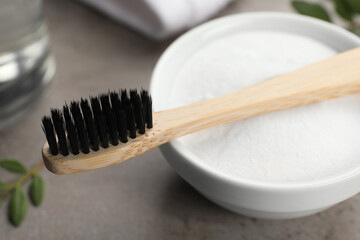 Bamboo toothbrush and bowl of baking soda on grey table, closeup
