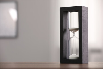 Hourglass with flowing sand on table against blurred background. Space for text