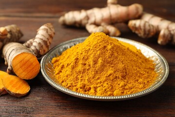 Plate with aromatic turmeric powder and cut roots on wooden table, closeup