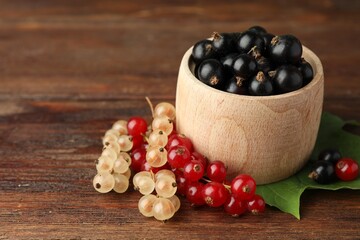 Different fresh ripe currants and green leaf on wooden table, closeup. Space for text