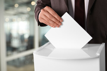 Man putting his vote into ballot box on blurred background, closeup