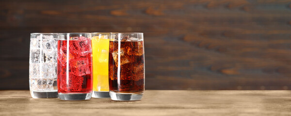 Tasty refreshing soda drinks with ice cubes on wooden table. Banner design with space for text