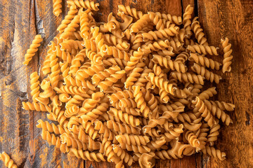 Raw whole grain fusilli pasta on rustic wooden kitchen table
