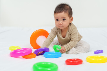 Fototapeta na wymiar infant baby playing the pyramid toy with colored rings on bed