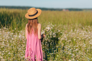 Portrait of girl in dress and straw hat on a chamomile field in summer