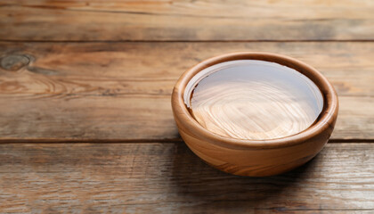 Bowl with clear water on wooden table. Space for text