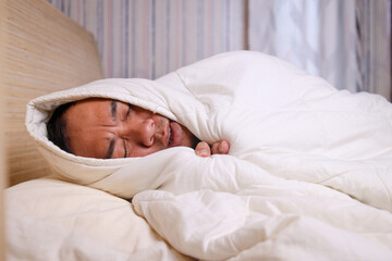 Asian man got fever covered with warm blanket on bed at home catching cold.