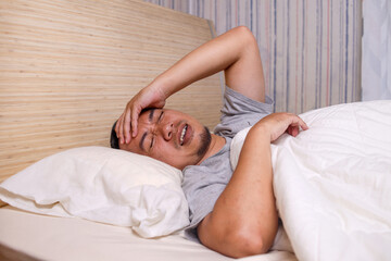 Asian man woke up on bed with headache or migraine.