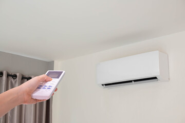 Hand pressing remote control air conditioner in room.