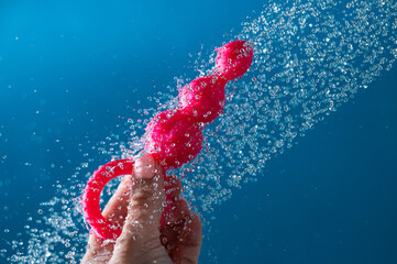Woman holding pink anal beads under running water on blue background. Sex toy hygiene concept.