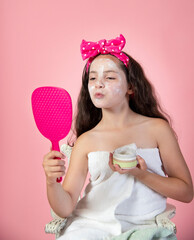 Little girl wearing skin care facial mask making kissy face at herself in the mirror  - 630949909