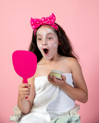 Young girl in beauty face mask with funny shocked expression looking at self in mirror - 630949911