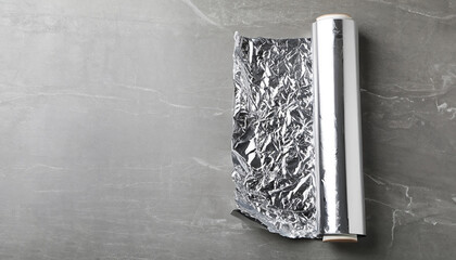 Roll of aluminum foil on grey table, top view. Space for text
