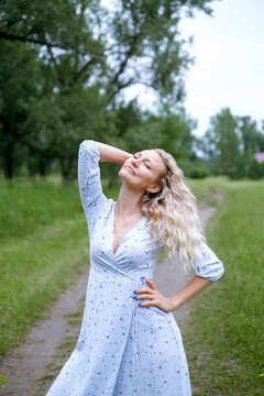 Portrait of blonde woman in a park. Young woman in blue vintage dress. Female walks in summer nature. Long hair.