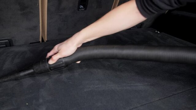 A woman's hand holds a vacuum cleaner hose and vacuums the interior of a car in the trunk of a station wagon. Detailing services.