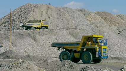 Yellow Industrial Dump Trucks Transporting Excavated Mineral Rocks To Conveyor. Industrial Dump Trucks For Transportation Of Mined Ore. Industrial Dump Truck Transports Working At Industrial Gold Mine