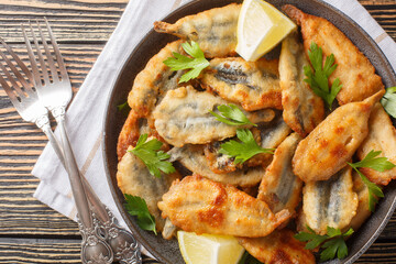 Fried breaded anchovy fillets served with lemon and herbs close-up on a plate on the table. Horizontal top view from above