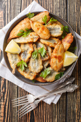 Fried anchovies served with lemon and herbs close-up on a plate on the table. Vertical top view from above