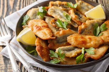 Fried breaded anchovy fillets served with lemon and herbs close-up on a plate on the table. Horizontal