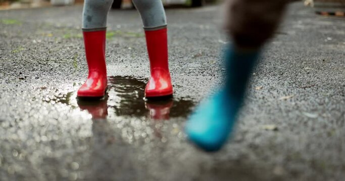 Children, feet and jumping in water puddle on winter holiday travel, happiness and joy together. Driveway, rain boots and playing on asphalt with splash, kids with energy and outdoor fun in Africa.