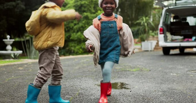 Children, driveway and jumping in water puddle on winter holiday travel, happiness and fun together. Siblings, rain boots and playing on asphalt with splash, kids with energy and vacation in Africa.