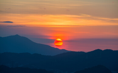 The orange-red sunset is covered by clouds as it moves towards the horizon. View of the urban landscape from Dajianshan Mountain, New Taipei City, Taiwan