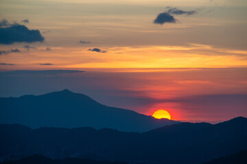 The orange-red sunset is covered by clouds as it moves towards the horizon. View of the urban landscape from Dajianshan Mountain, New Taipei City, Taiwan