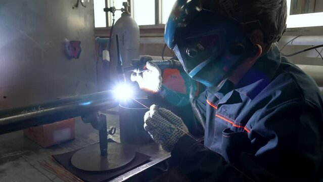 Welder is fabricating the steel pipes at the production facility. Welder is using a specialised tool to produce pipe at the factory. Welder in a safety helmet is fusing the pipe in the production room