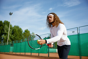 Concentrated male tennis player with racket and ball training on outdoor court
