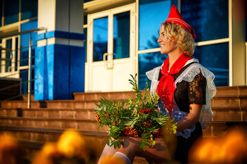 Girl in black school uniform, white apron and red tie on steps of school with bouquet of flowers. Nostalgia photo shoot of teenager of female pioneer from USSR costume for September 1 or graduation