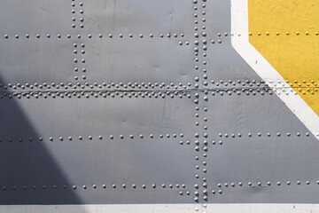 Riveted with button-head rivets metal plate - side of an aircraft - painted in gray, white and...