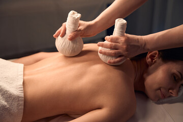 Obraz na płótnie Canvas Woman dozing during hot compress massage performed by massotherapist