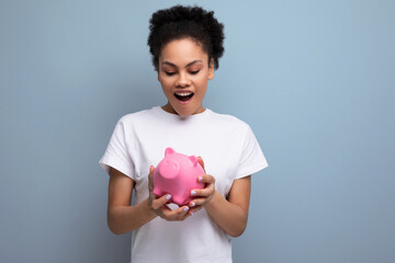Fototapeta na wymiar young happy hispanic brunette woman saving money for a dream in a pink piggy bank