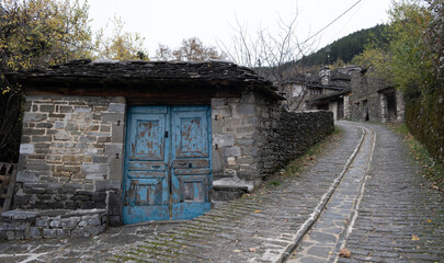 Fototapeta na wymiar Old stone building with aged wooden blue door, stone roof, paved street Epirus Greece, winter day.
