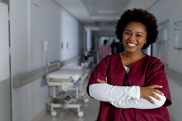 Portrait of happy african american female doctor wearing scrubs in corridor at hospital, copy space