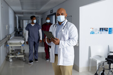 Portrait of biracial male doctor wearing face mask in corridor at hospital