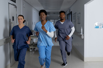 Diverse doctors wearing scrubs running through corridor at hospital