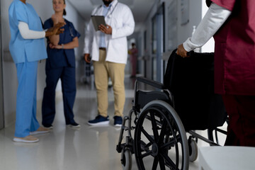 Obraz premium African american female doctor walking with wheelchair in corridor at hospital