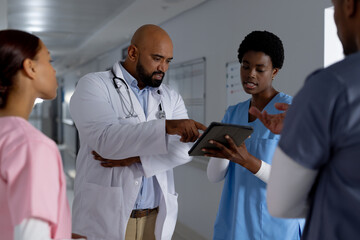 Diverse doctors using tablet and discussing work in corridor at hospital