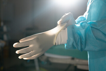 Midsection of biracial female surgeon wearing surgical gown and gloves in operating theatre - Powered by Adobe