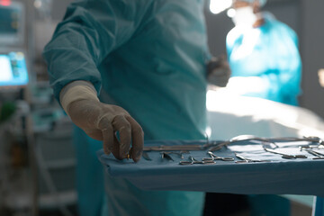 Midsection of biracial male surgeon holding instruments in operating theatre at hospital