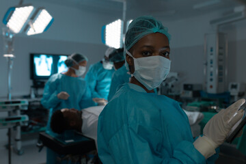 Portrait of african american female surgeon wearing surgical gown in operating theatre at hospital - Powered by Adobe