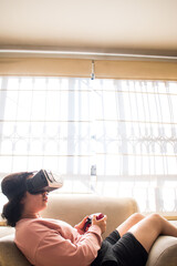 Gamer playing on vr headset with video game controller sitting on sofa