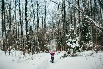 8 years old girl throwing snow in the air in a winter forest scene