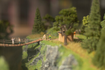 Toy model of park. People on bridge. Tourists in mountains in summer.