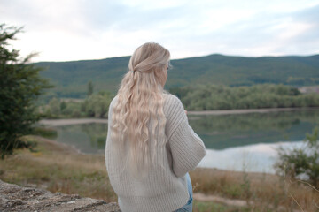 Back view of  the blond woman dressed sweater and jeans., Walking in the shore of the lake with beautiful landskape. The girl enjoy the nature  in her trip