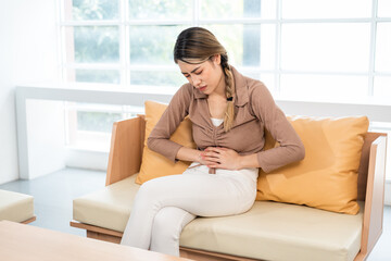 Sick woman with hands holding pressing her crotch lower abdomen. Asian woman suffering from abdominal pain while sitting on sofa at home