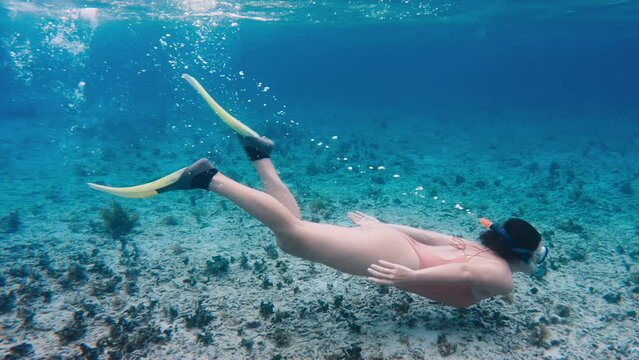 Beautiful underwater footage of a girl wearing pink bikini diving with snorkel mask and fins. Woman swimming undersea while snorkeling in clear water of tropical ocean. Graceful movements of female
